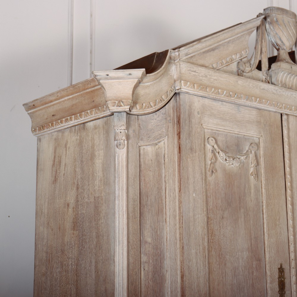 A Dutch bleached oak linen cupboard featuring a top pediment with a carved urn, two panelled doors decorated with carved swags, and three lower drawers resting on claw feet. View IX