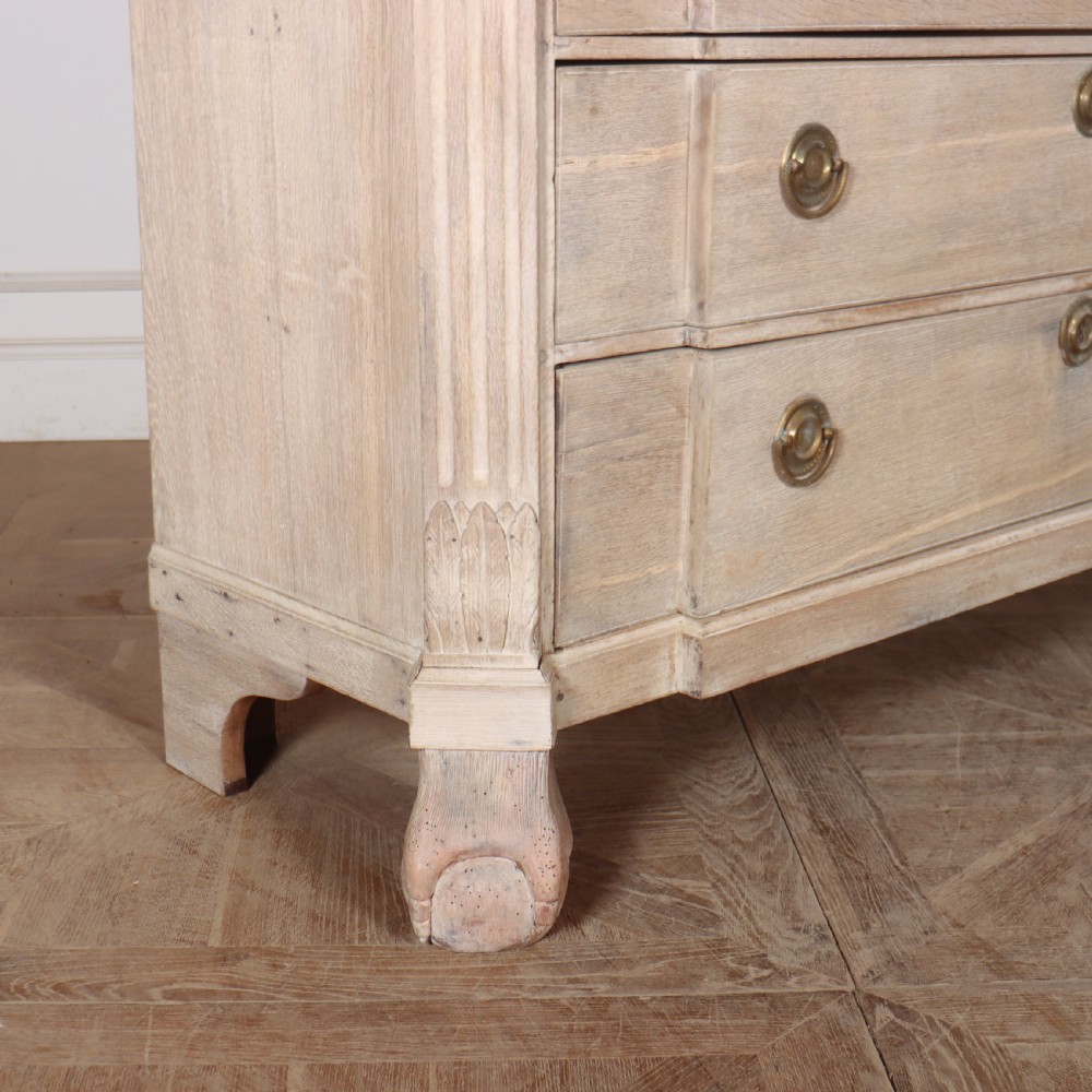 A Dutch bleached oak linen cupboard featuring a top pediment with a carved urn, two panelled doors decorated with carved swags, and three lower drawers resting on claw feet. View XI