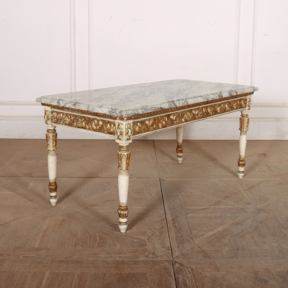 A rectangular French Louis XVI style low coffee table featuring a grey and white veined marble top set on a carved giltwood and painted frame with fluted tapered legs.