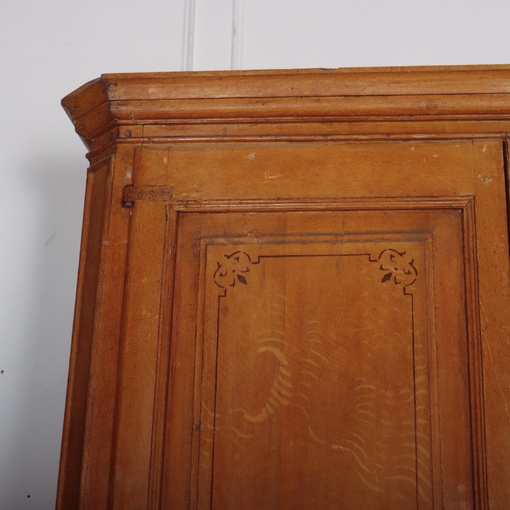 An antique freestanding pine linen cupboard featuring two panelled upper doors decorated with painted corner flourishes above two full-width lower drawers. View II