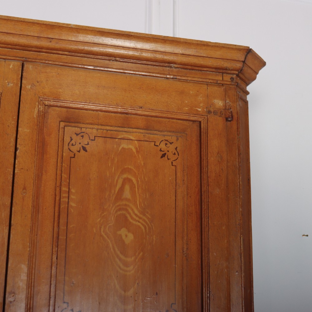 An antique freestanding pine linen cupboard featuring two panelled upper doors decorated with painted corner flourishes above two full-width lower drawers. View III