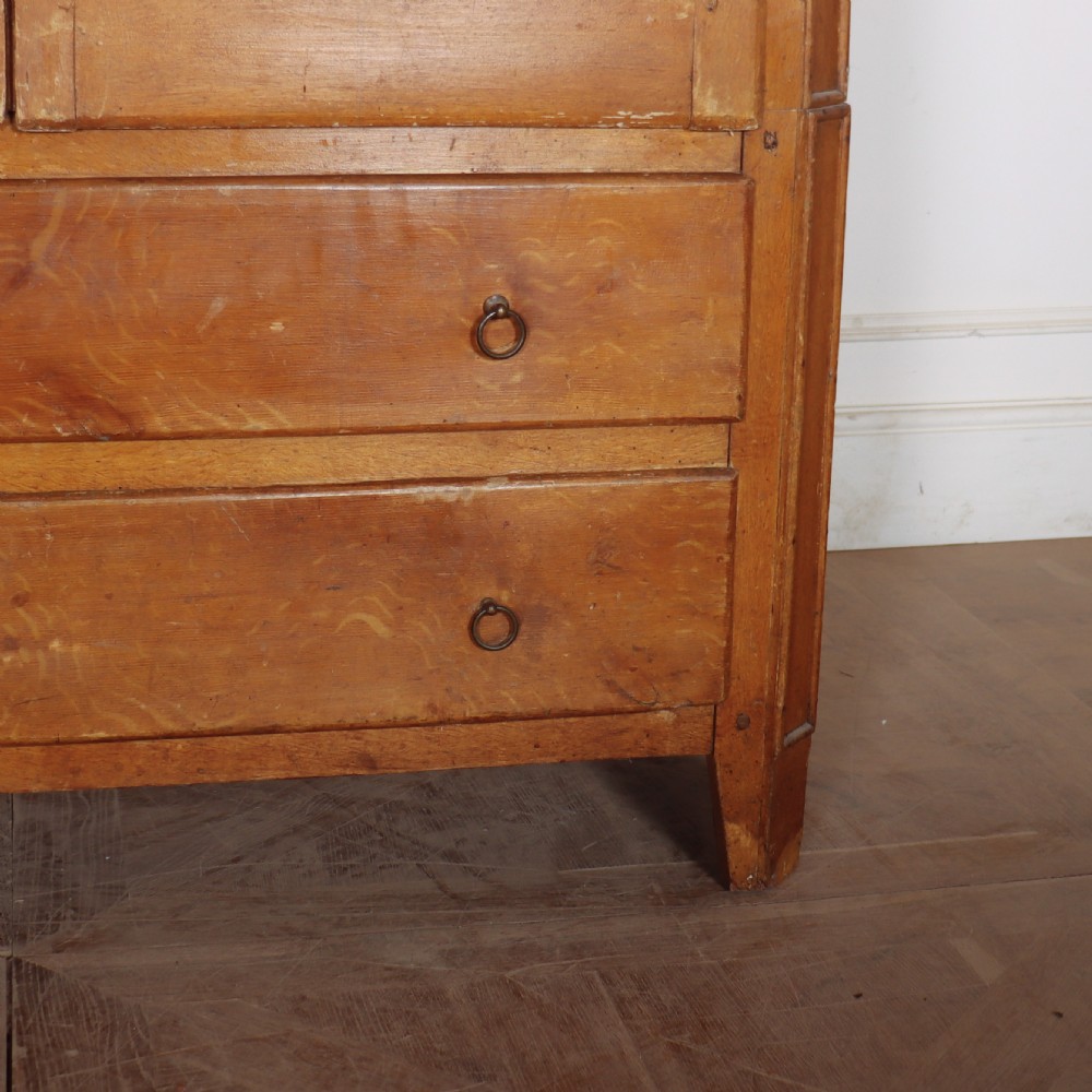An antique freestanding pine linen cupboard featuring two panelled upper doors decorated with painted corner flourishes above two full-width lower drawers. View IV