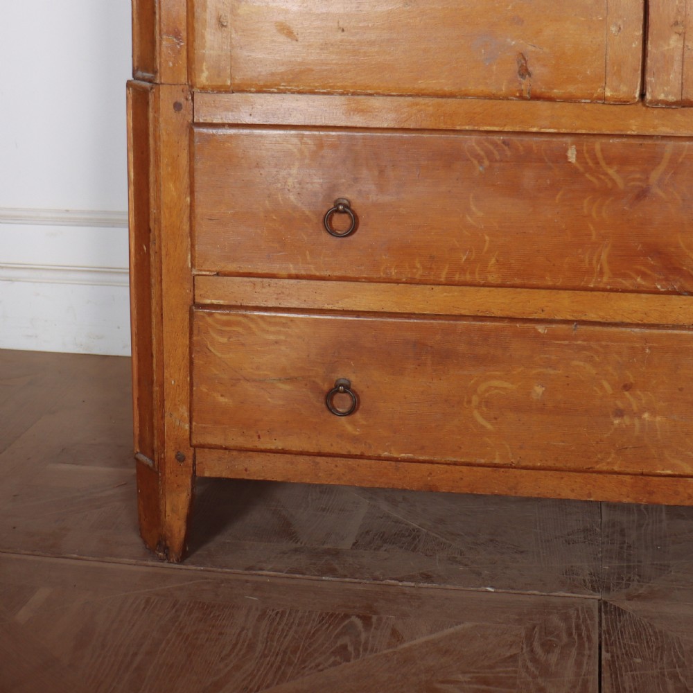An antique freestanding pine linen cupboard featuring two panelled upper doors decorated with painted corner flourishes above two full-width lower drawers. View V