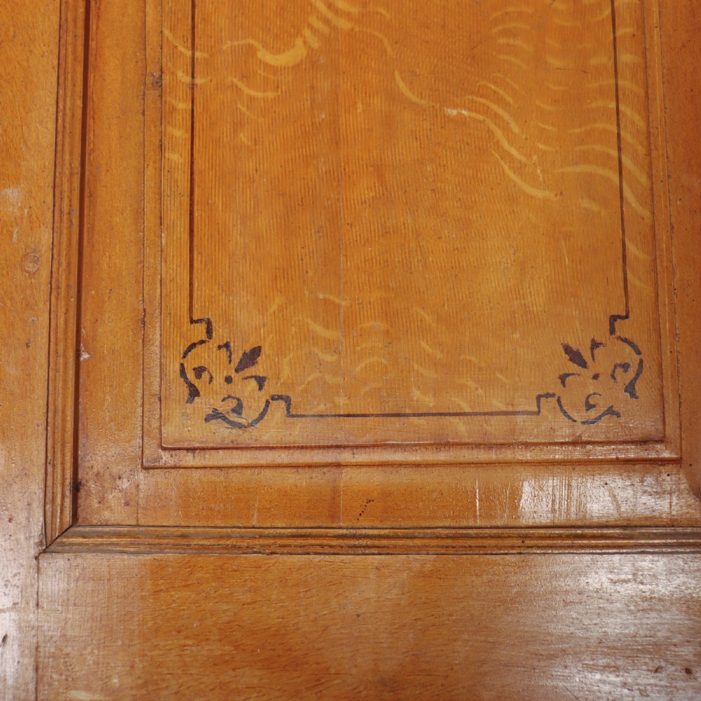 An antique freestanding pine linen cupboard featuring two panelled upper doors decorated with painted corner flourishes above two full-width lower drawers. View VI