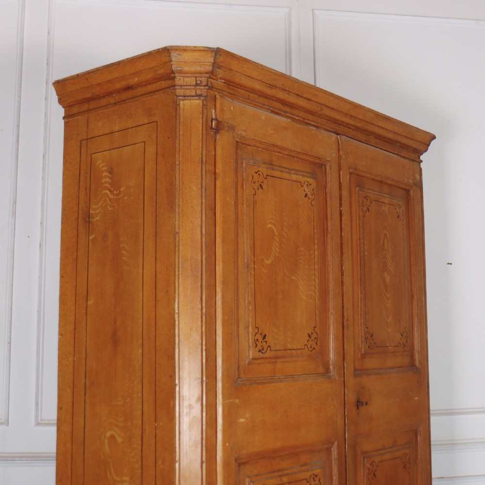 An antique freestanding pine linen cupboard featuring two panelled upper doors decorated with painted corner flourishes above two full-width lower drawers. View X