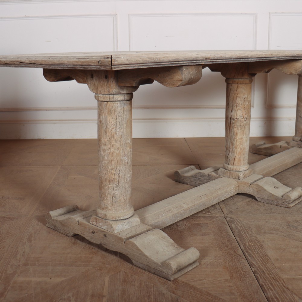 A long rectangular bleached oak trestle table featuring three column support legs and scrolled feet. View II