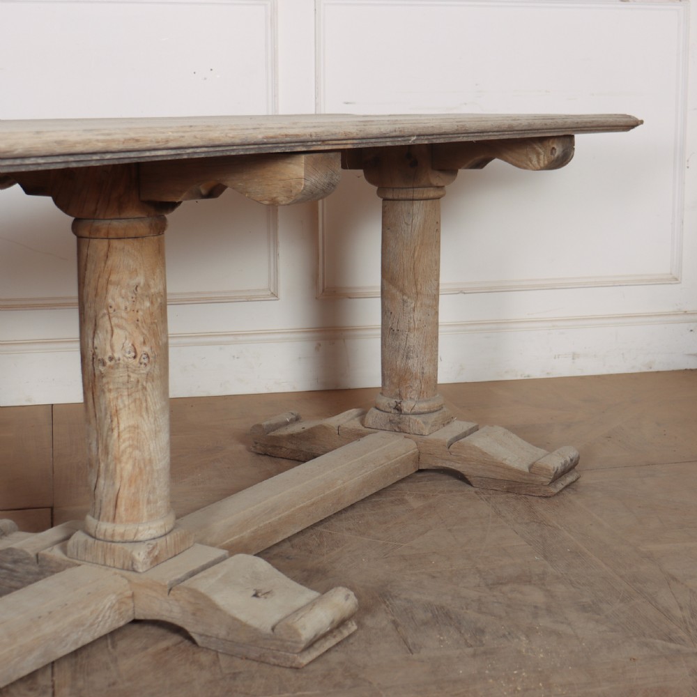 A long rectangular bleached oak trestle table featuring three column support legs and scrolled feet. View IV