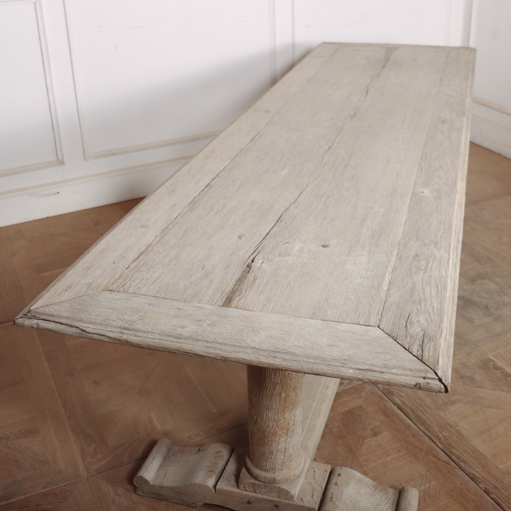 A long rectangular bleached oak trestle table featuring three column support legs and scrolled feet. View V