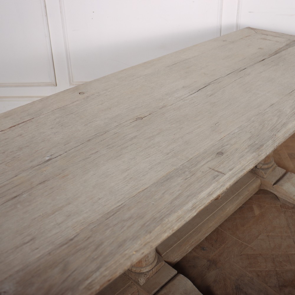 A long rectangular bleached oak trestle table featuring three column support legs and scrolled feet. View VI
