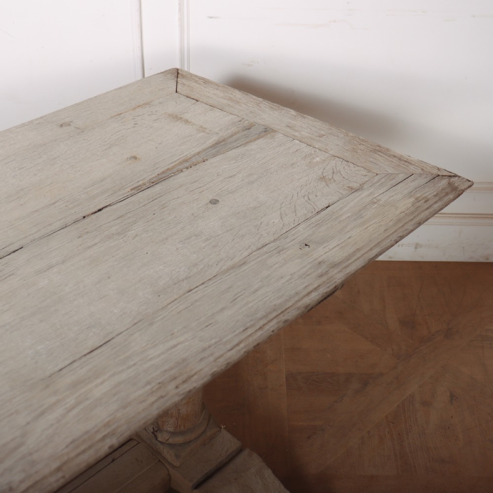 A long rectangular bleached oak trestle table featuring three column support legs and scrolled feet. View VII
