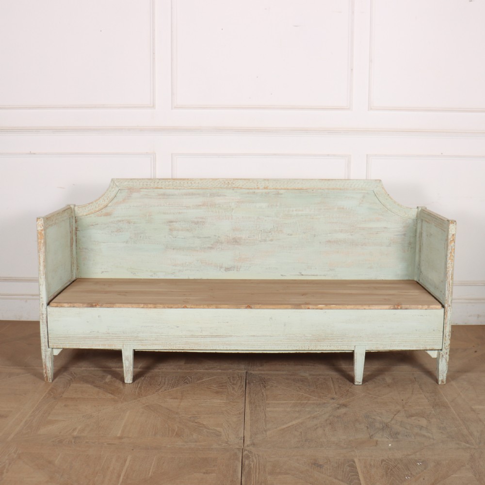 A pale green painted Swedish wooden bench featuring a shaped crest rail, panelled sides, and a natural pine seat.