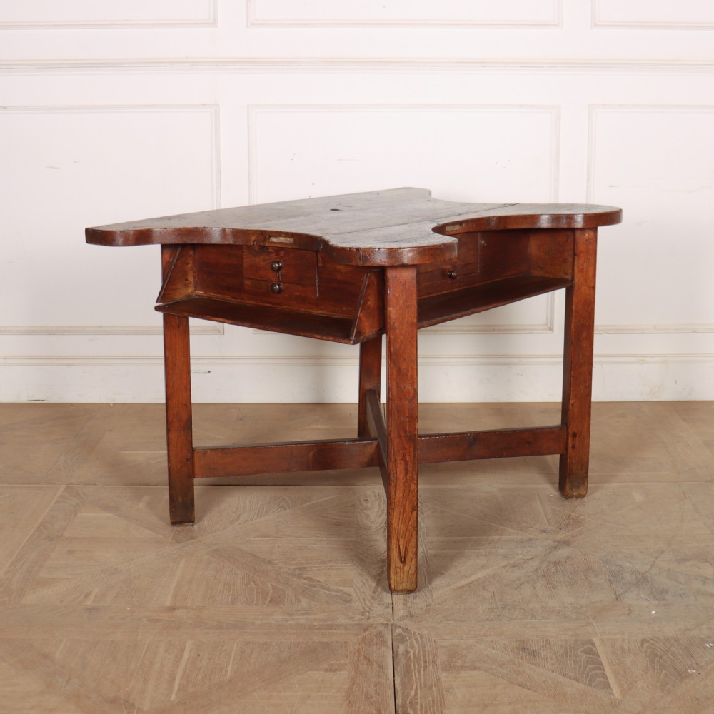 A nineteenth-century French wooden watchmakers table featuring a contoured ergonomic front cut-out, small drawers, and cross-braced square legs.