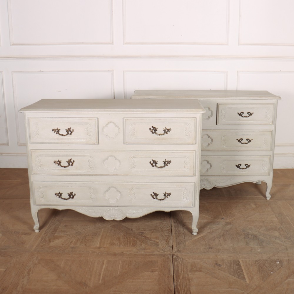 A pair of light cream painted French commodes featuring three drawers each, detailed with brass handles, carved apron shells, and cabriole legs.