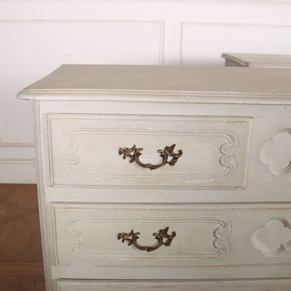 A pair of light cream painted French commodes featuring three drawers each, detailed with brass handles, carved apron shells, and cabriole legs. View II