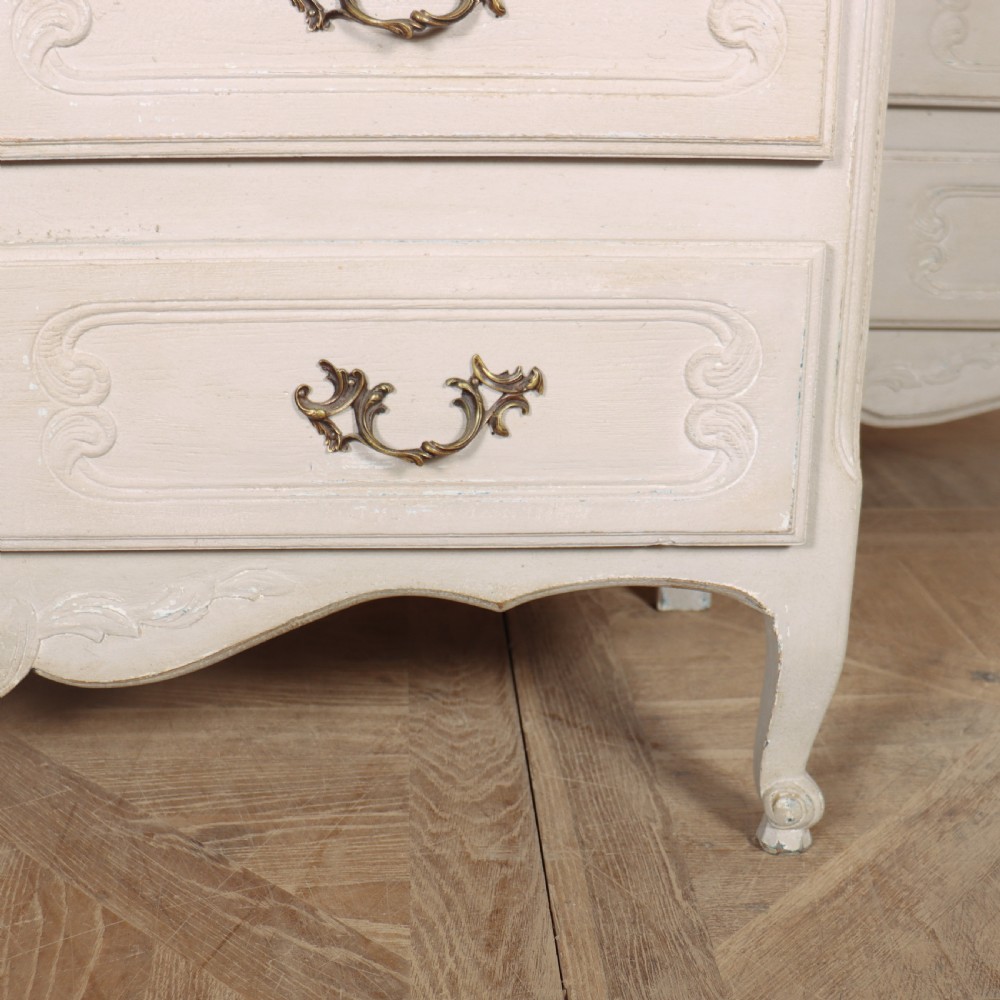 A pair of light cream painted French commodes featuring three drawers each, detailed with brass handles, carved apron shells, and cabriole legs. View V