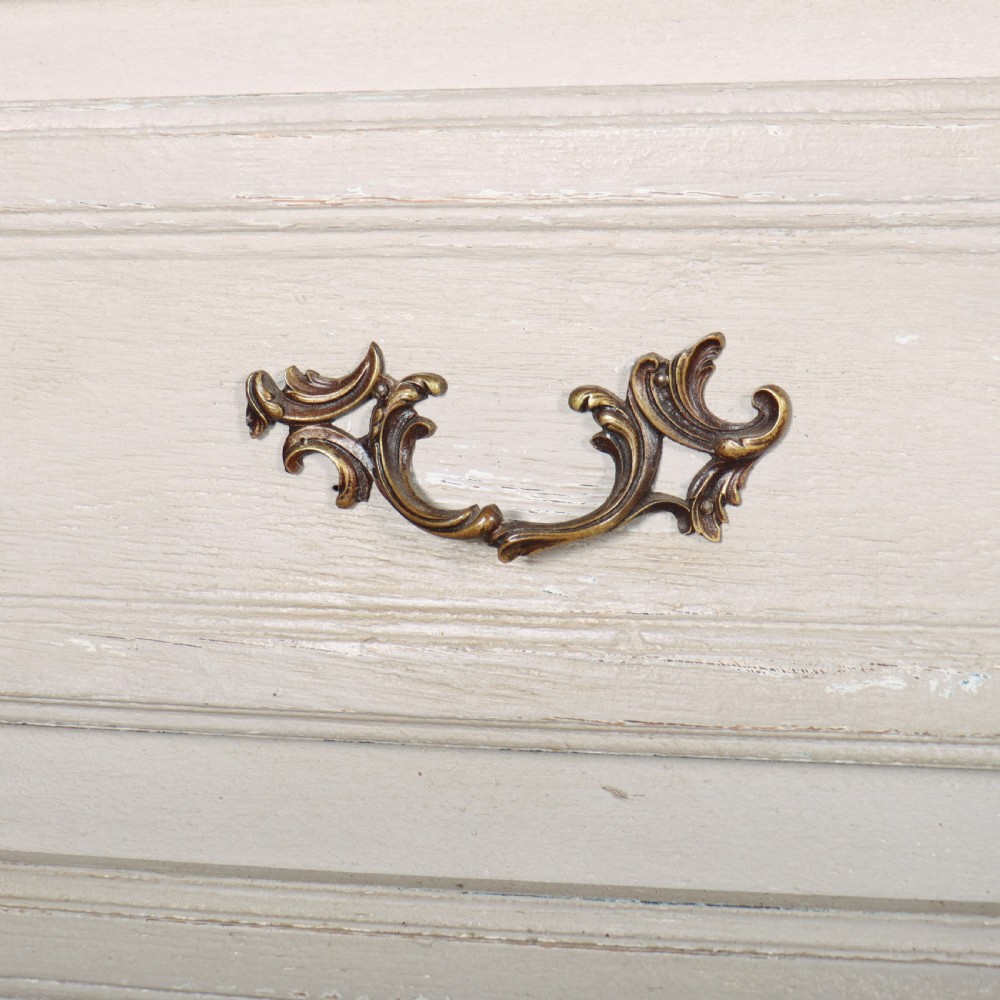 A pair of light cream painted French commodes featuring three drawers each, detailed with brass handles, carved apron shells, and cabriole legs. View VI