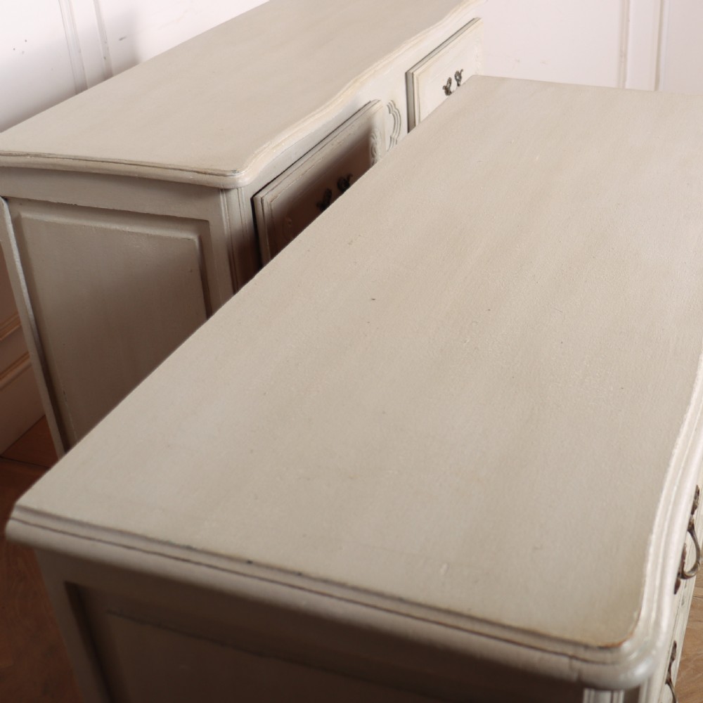 A pair of light cream painted French commodes featuring three drawers each, detailed with brass handles, carved apron shells, and cabriole legs. View VIII
