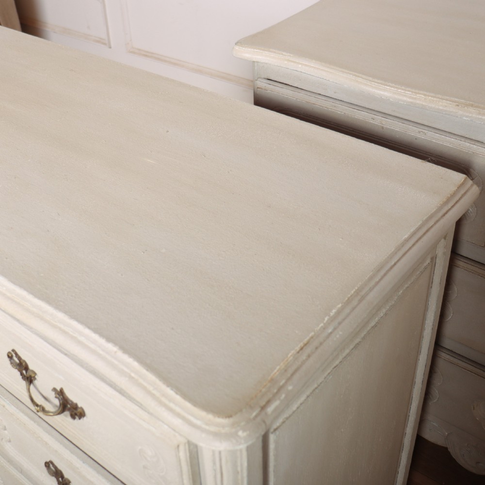 A pair of light cream painted French commodes featuring three drawers each, detailed with brass handles, carved apron shells, and cabriole legs. View IX