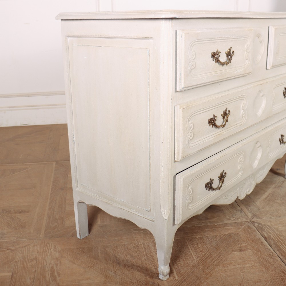 A pair of light cream painted French commodes featuring three drawers each, detailed with brass handles, carved apron shells, and cabriole legs. View X