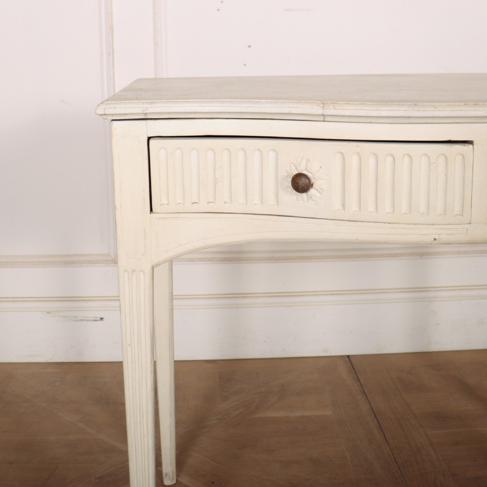 An off-white painted French side table with a serpentine front, fluted double drawer panels, and tapered square legs. View IV