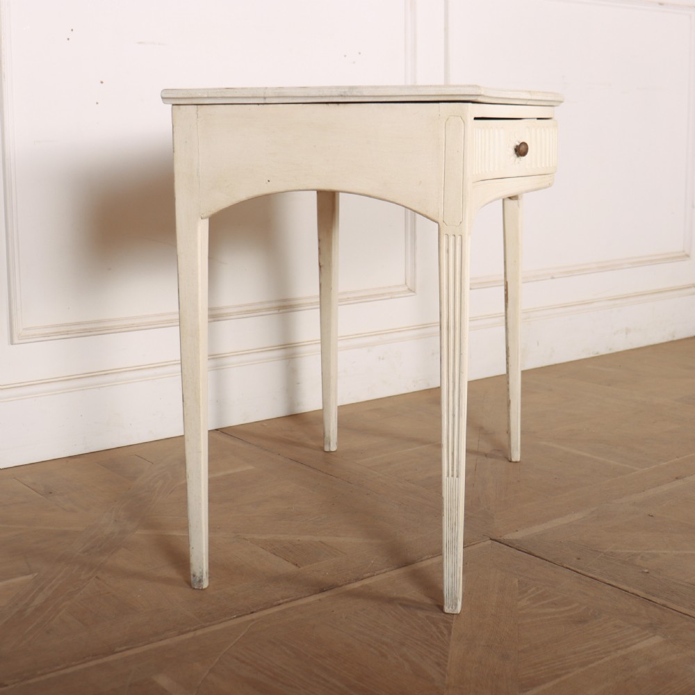 An off-white painted French side table with a serpentine front, fluted double drawer panels, and tapered square legs. View V