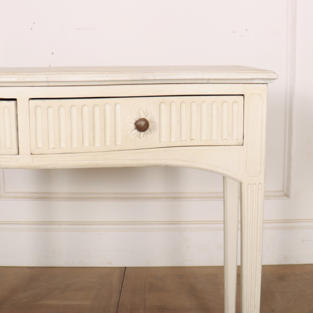 An off-white painted French side table with a serpentine front, fluted double drawer panels, and tapered square legs. View VI