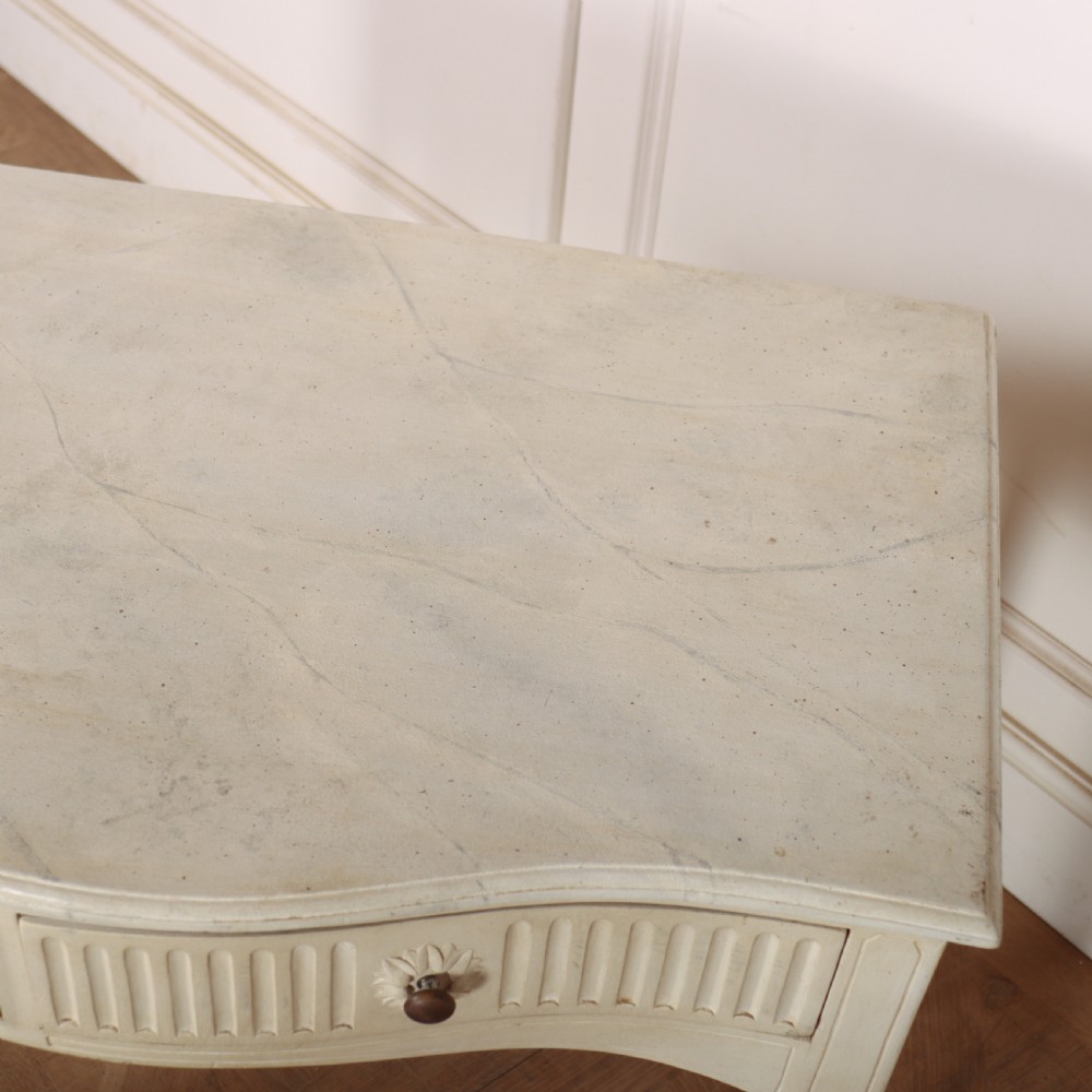 An off-white painted French side table with a serpentine front, fluted double drawer panels, and tapered square legs. View VII