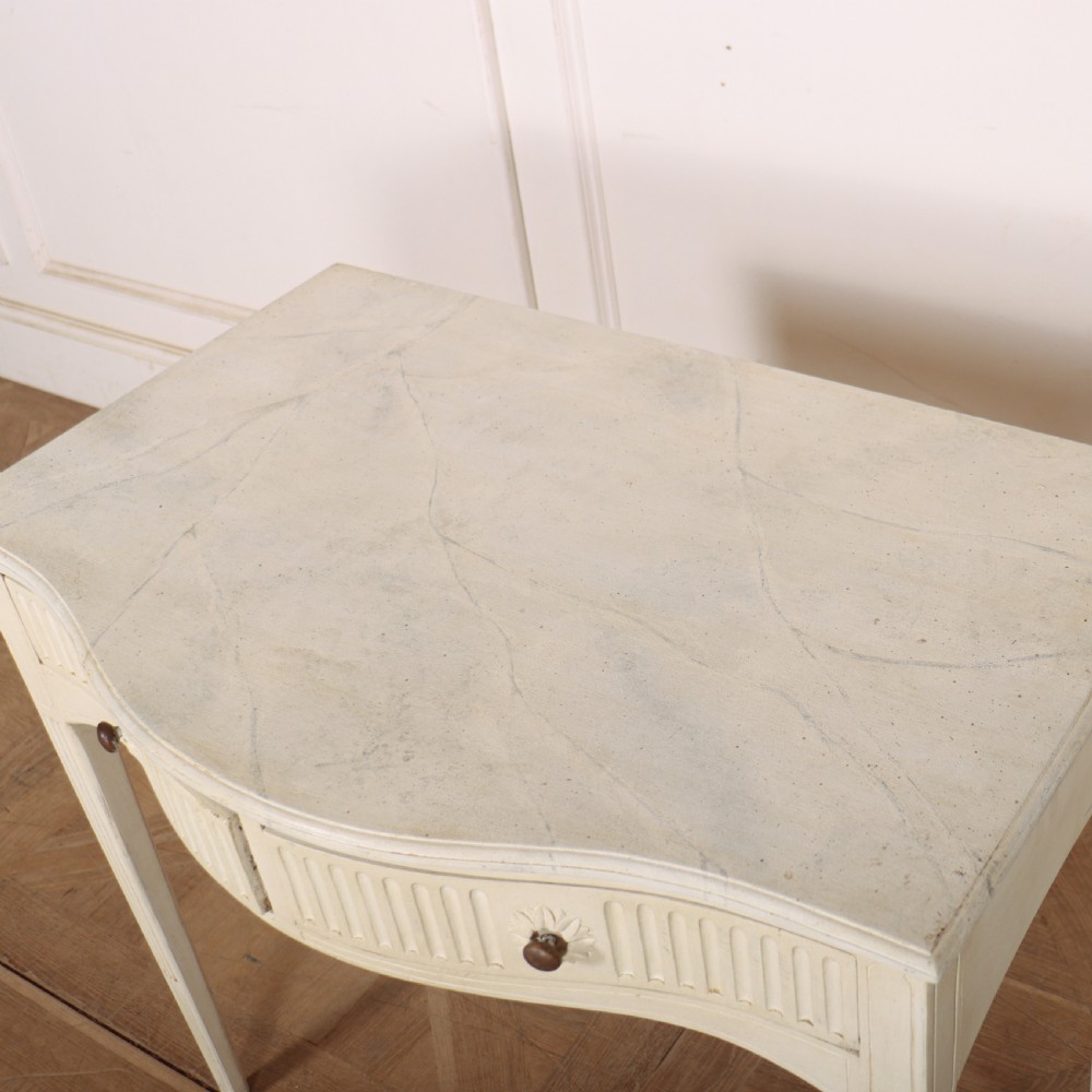 An off-white painted French side table with a serpentine front, fluted double drawer panels, and tapered square legs. View VIII