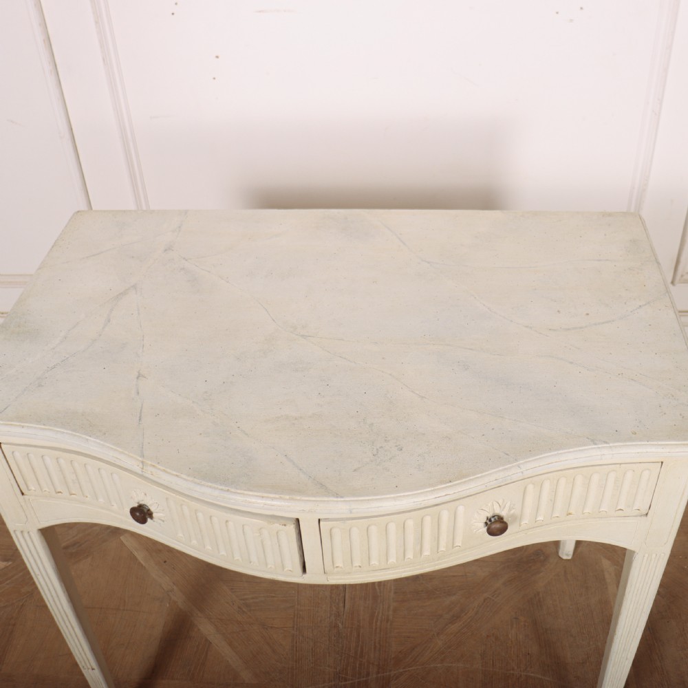An off-white painted French side table with a serpentine front, fluted double drawer panels, and tapered square legs. View IX