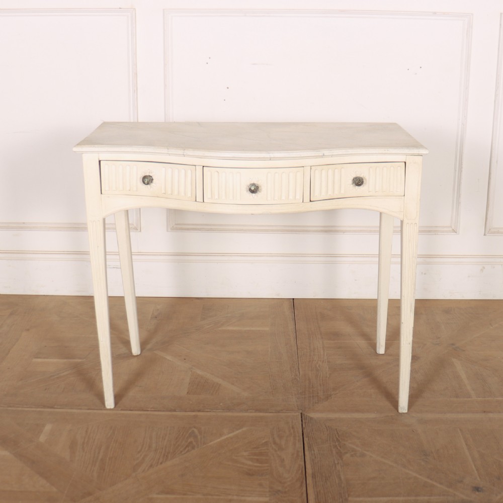 A 19th-century French off-white painted side table featuring a gentle curved front, three fluted drawers, tapered legs, and a marble top.