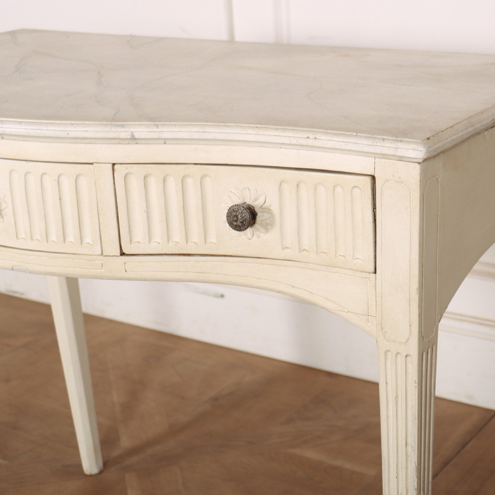 A 19th-century French off-white painted side table featuring a gentle curved front, three fluted drawers, tapered legs, and a marble top. View III