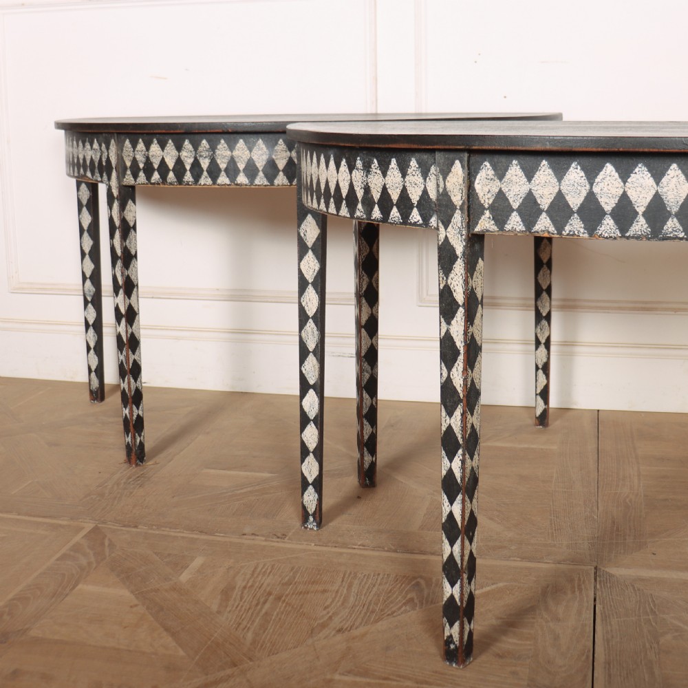 A pair of semi-circular painted timber console tables decorated with a black and white diamond harlequin pattern along the aprons and tapered legs. View II