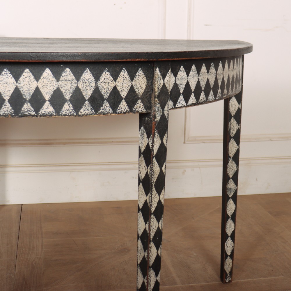 A pair of semi-circular painted timber console tables decorated with a black and white diamond harlequin pattern along the aprons and tapered legs. View III