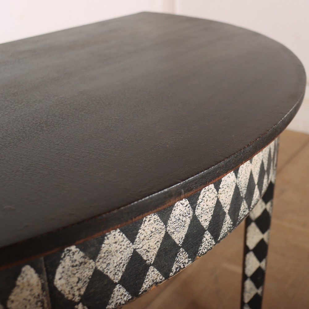 A pair of semi-circular painted timber console tables decorated with a black and white diamond harlequin pattern along the aprons and tapered legs. View VI