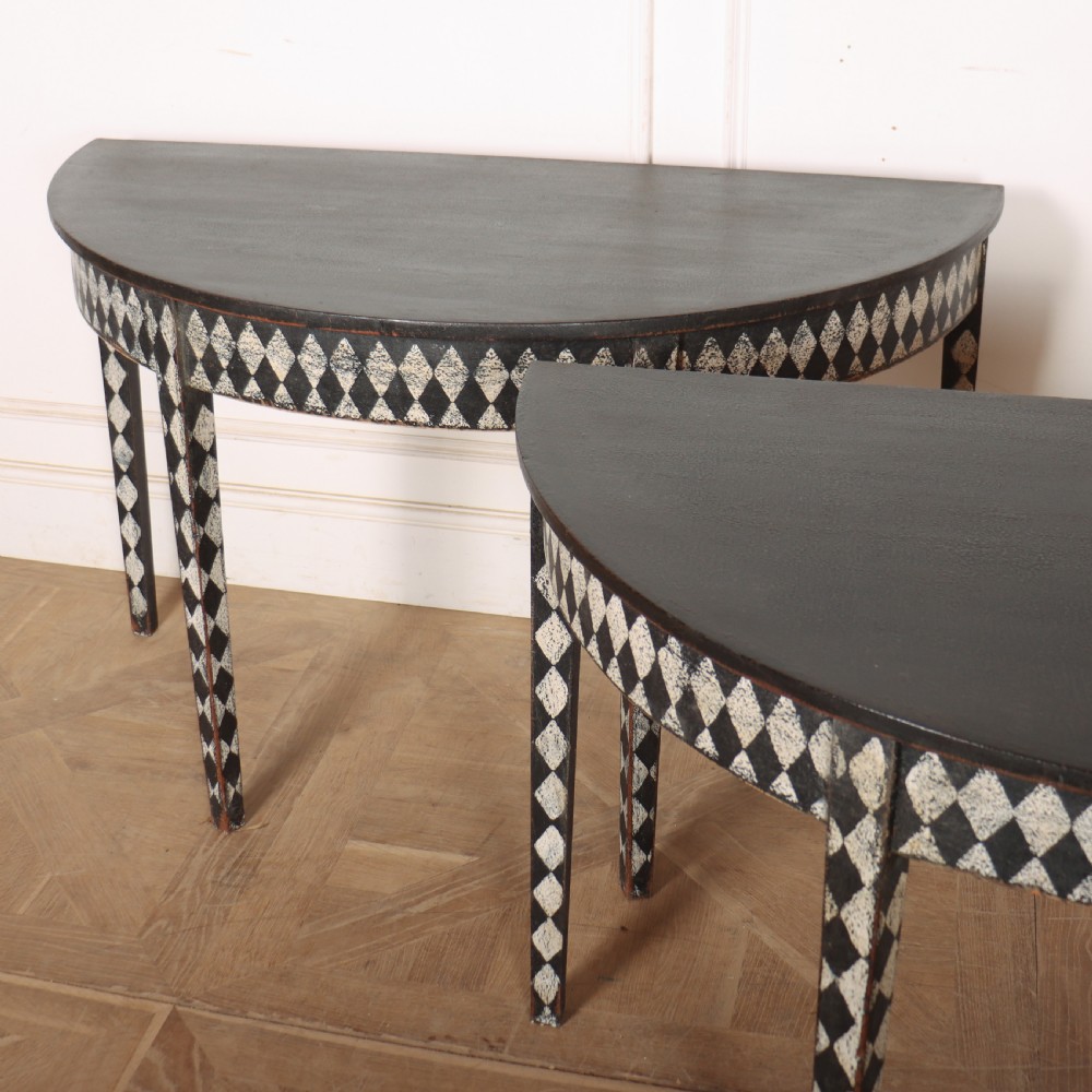 A pair of semi-circular painted timber console tables decorated with a black and white diamond harlequin pattern along the aprons and tapered legs. View VII
