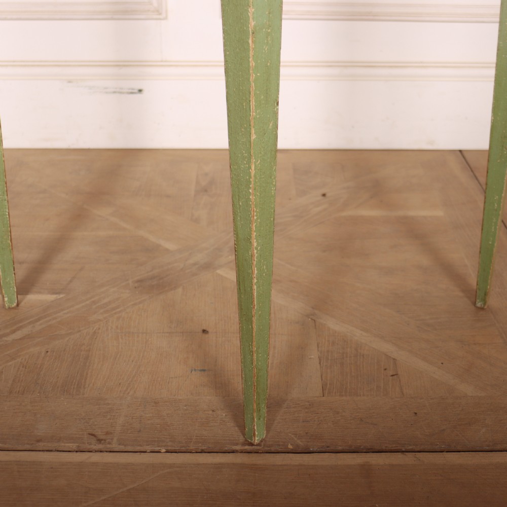 A semi-circular green painted wooden console table featuring three tapered legs and a scalloped apron against a white wall. View IV