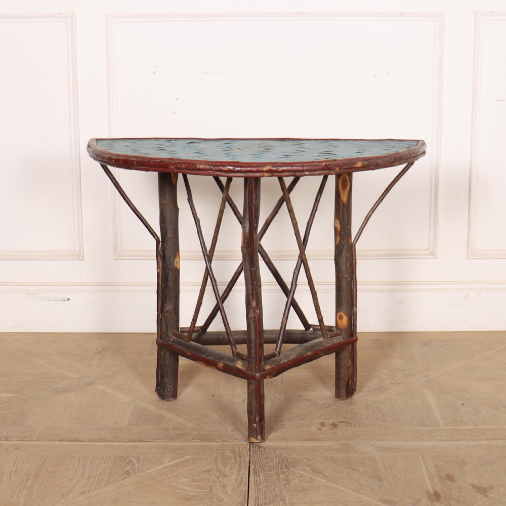 A demilune console table crafted from unpeeled rustic tree branches with a patterned teal painted top.