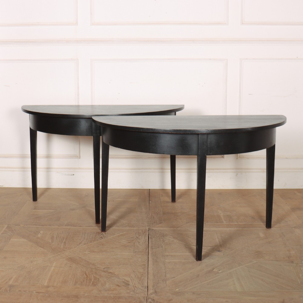 A pair of semi-circular ebonised wooden demi-lune console tables with plain aprons and square tapered legs.