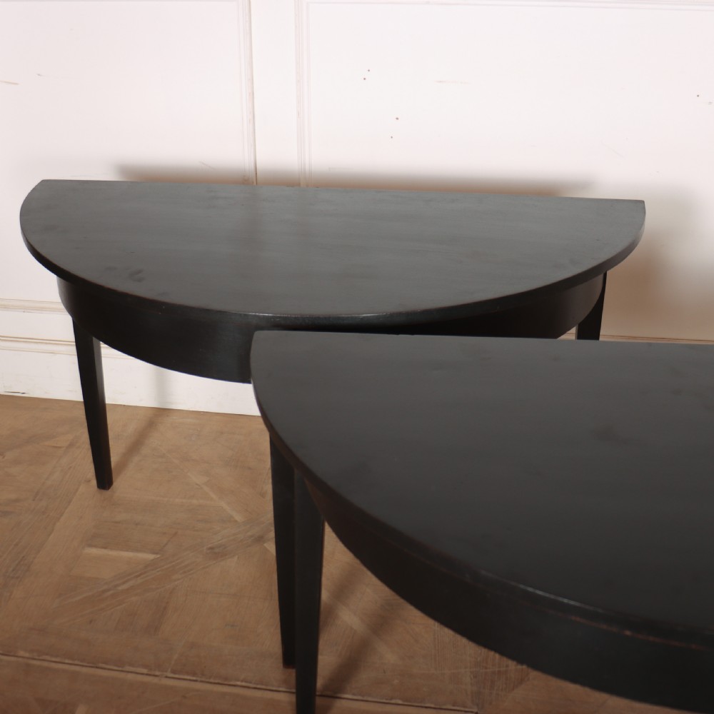 A pair of semi-circular ebonised wooden demi-lune console tables with plain aprons and square tapered legs. View IV