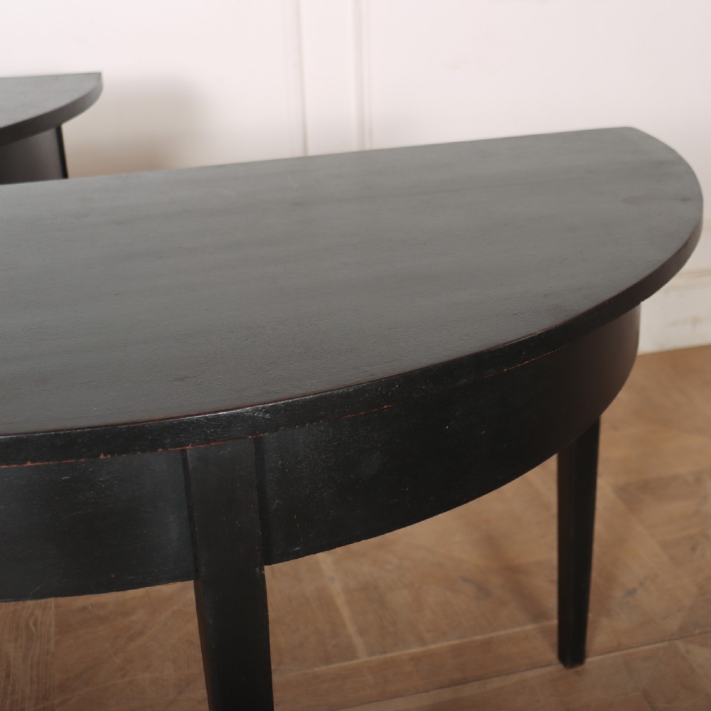 A pair of semi-circular ebonised wooden demi-lune console tables with plain aprons and square tapered legs. View V