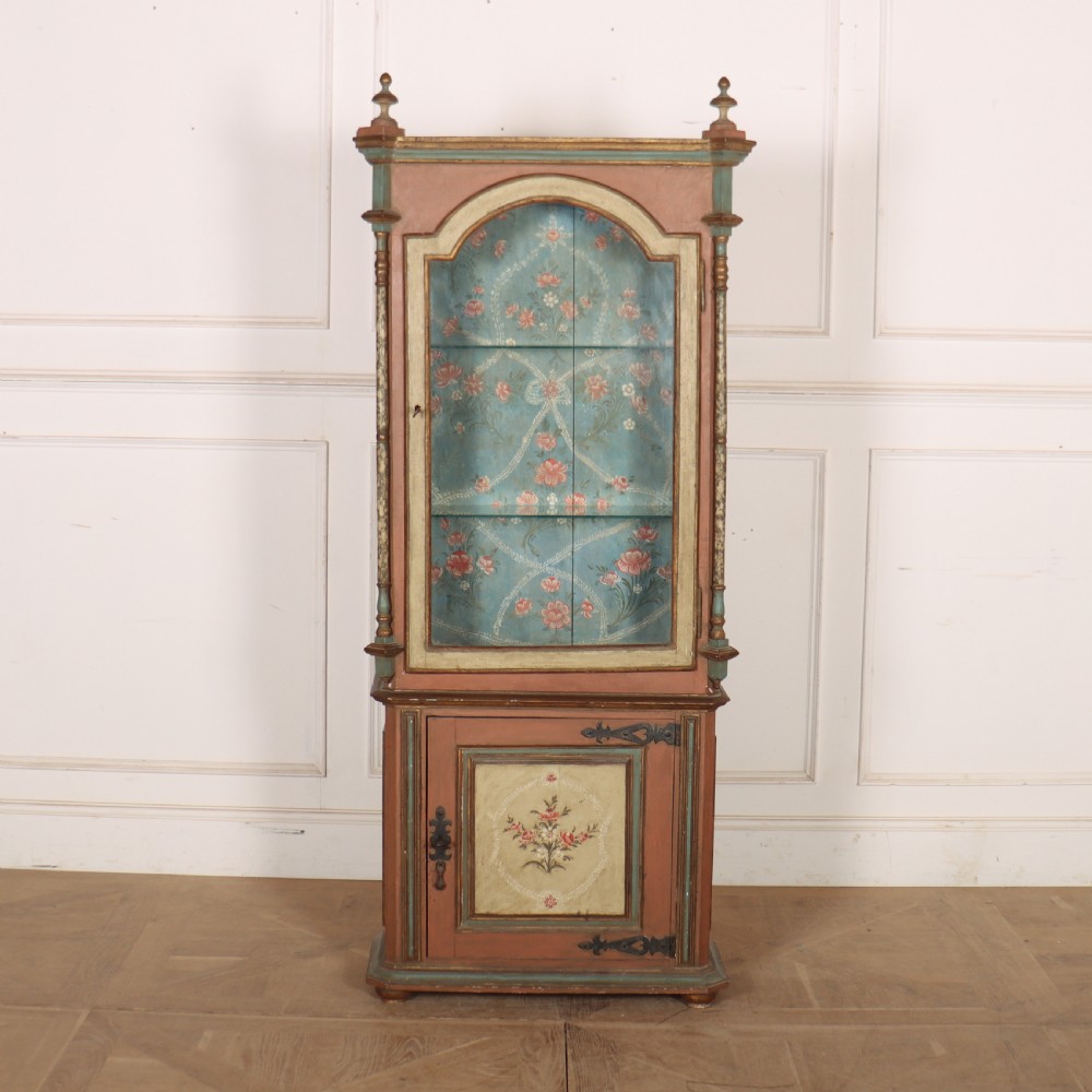 A tall nineteenth-century Italian painted two-tier cabinet featuring a glazed upper display section with a blue floral painted background and a lower solid cupboard door decorated with a painted floral motif.