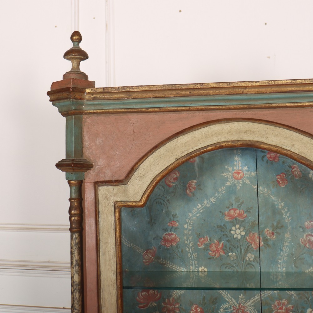 A tall nineteenth-century Italian painted two-tier cabinet featuring a glazed upper display section with a blue floral painted background and a lower solid cupboard door decorated with a painted floral motif. View II