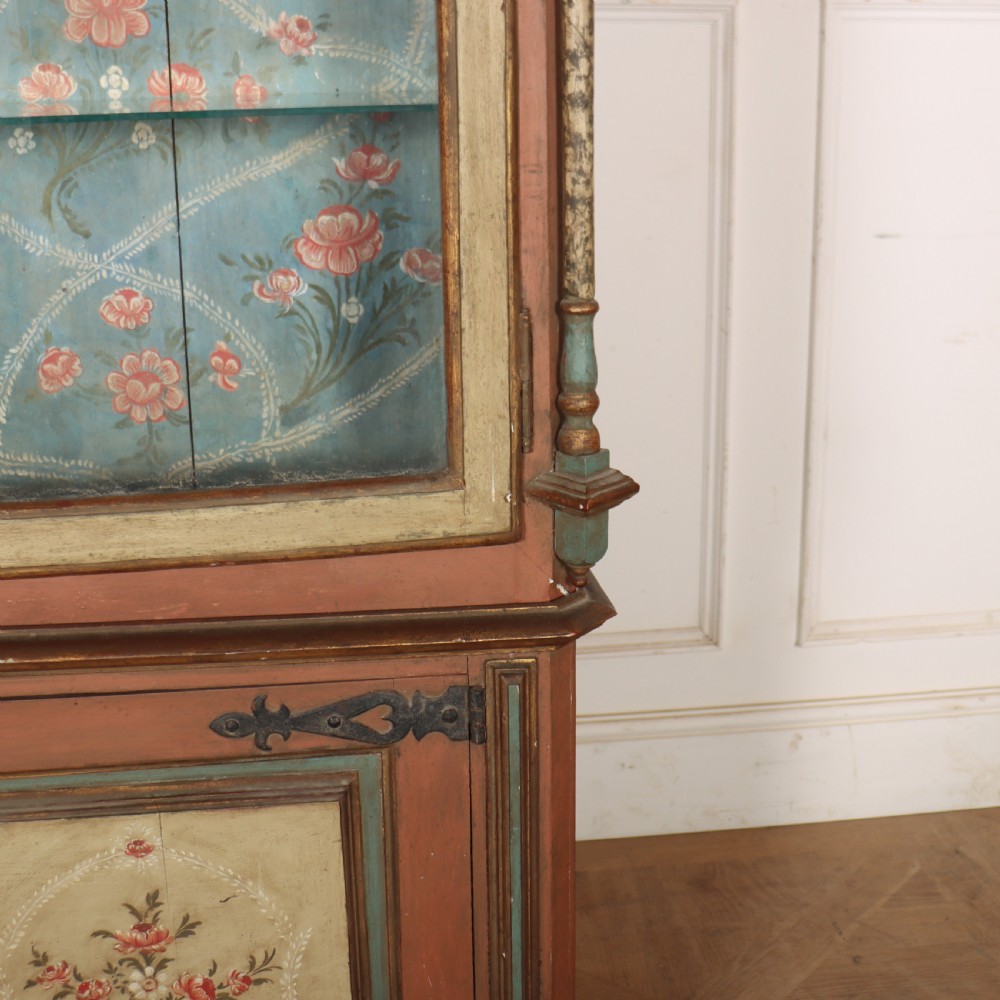 A tall nineteenth-century Italian painted two-tier cabinet featuring a glazed upper display section with a blue floral painted background and a lower solid cupboard door decorated with a painted floral motif. View III
