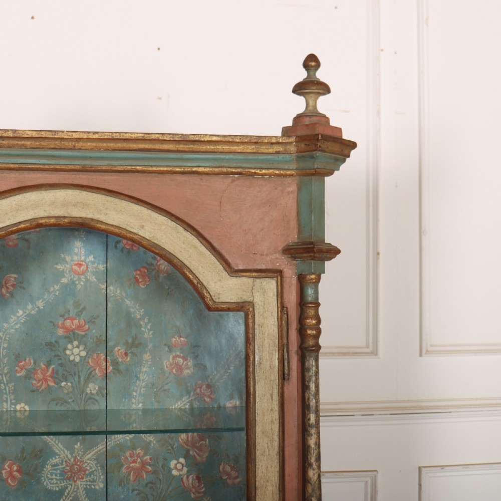 A tall nineteenth-century Italian painted two-tier cabinet featuring a glazed upper display section with a blue floral painted background and a lower solid cupboard door decorated with a painted floral motif. View IV