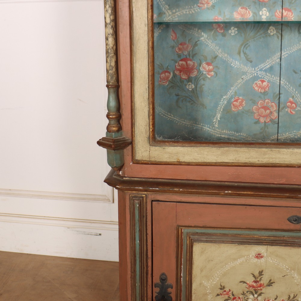 A tall nineteenth-century Italian painted two-tier cabinet featuring a glazed upper display section with a blue floral painted background and a lower solid cupboard door decorated with a painted floral motif. View V