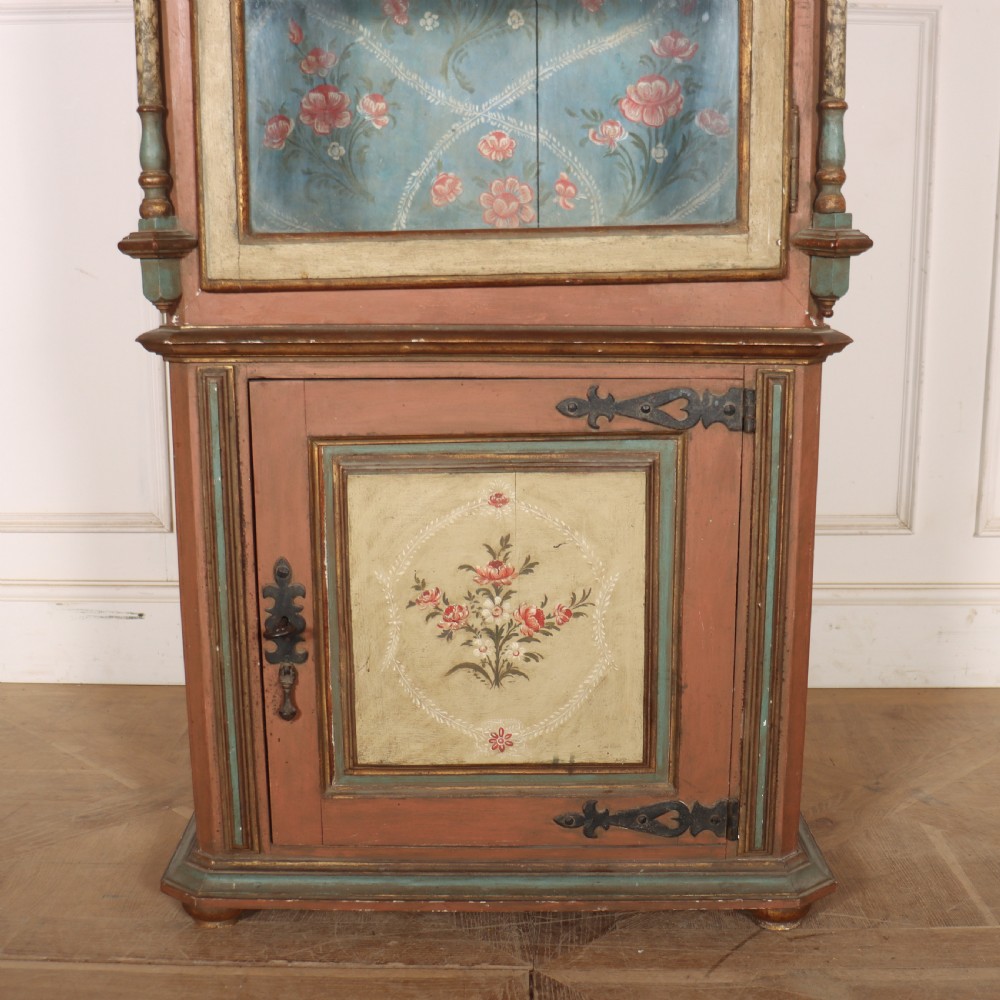 A tall nineteenth-century Italian painted two-tier cabinet featuring a glazed upper display section with a blue floral painted background and a lower solid cupboard door decorated with a painted floral motif. View VI
