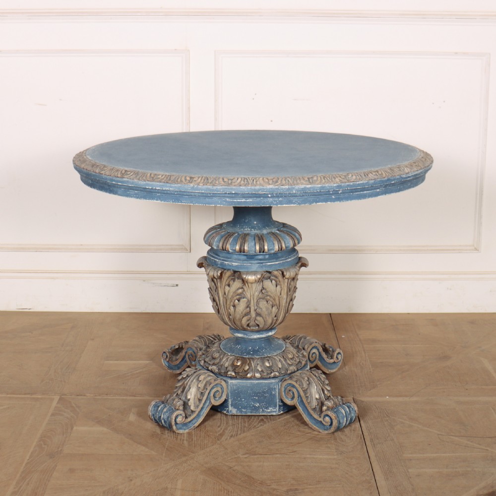 A circular 1920s German centre table featuring a distressed slate blue painted finish, gilt carved acanthus leaf pedestal, and scroll feet.