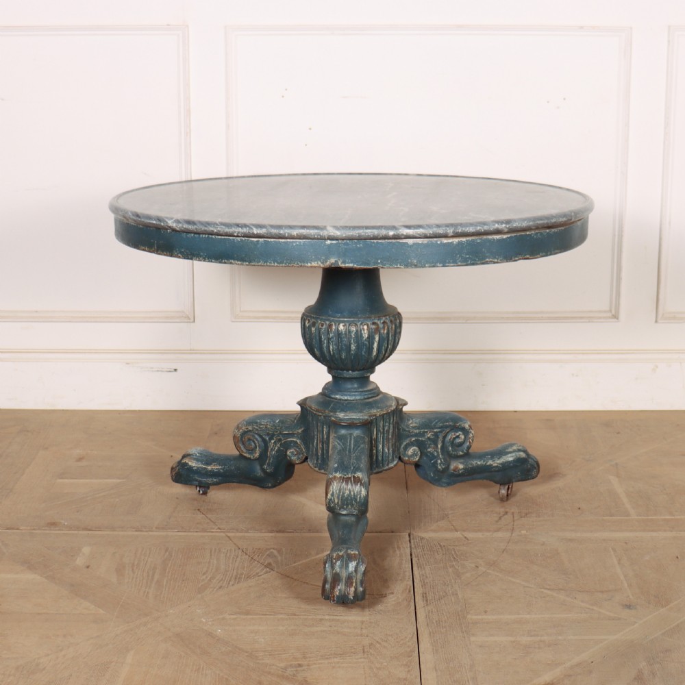 A circular French gueridon table featuring a grey marble top and a distressed blue painted pedestal base resting on carved scroll feet.
