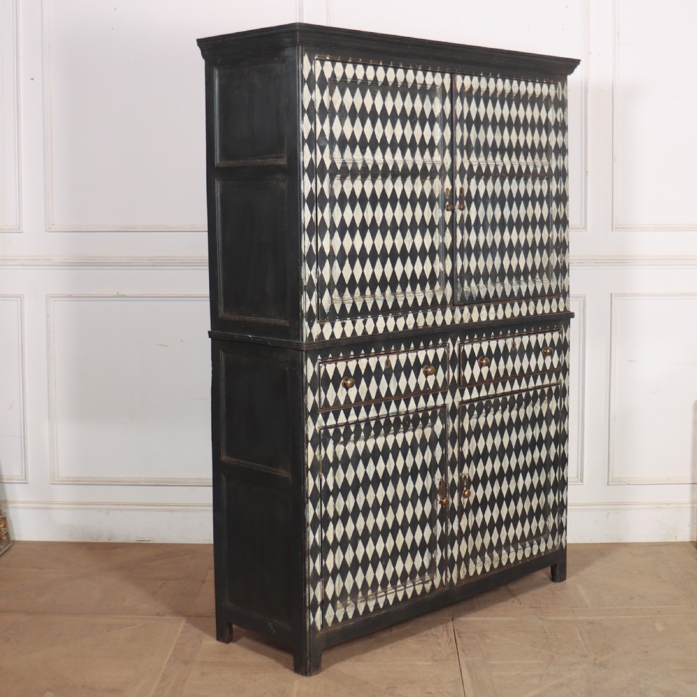 A tall English painted wooden linen cupboard featuring a black and cream harlequin diamond pattern across the front doors and drawers.