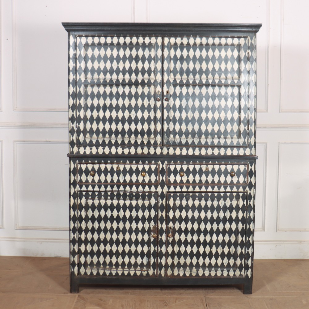 A tall English painted wooden linen cupboard featuring a black and cream harlequin diamond pattern across the front doors and drawers. View II